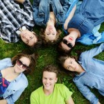 6 people lying on their backs in the grass with their heads pointing in to the center of a circle