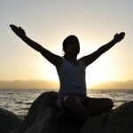 Girl on beach back to sunset with arms up and out. Credit GraphicStock