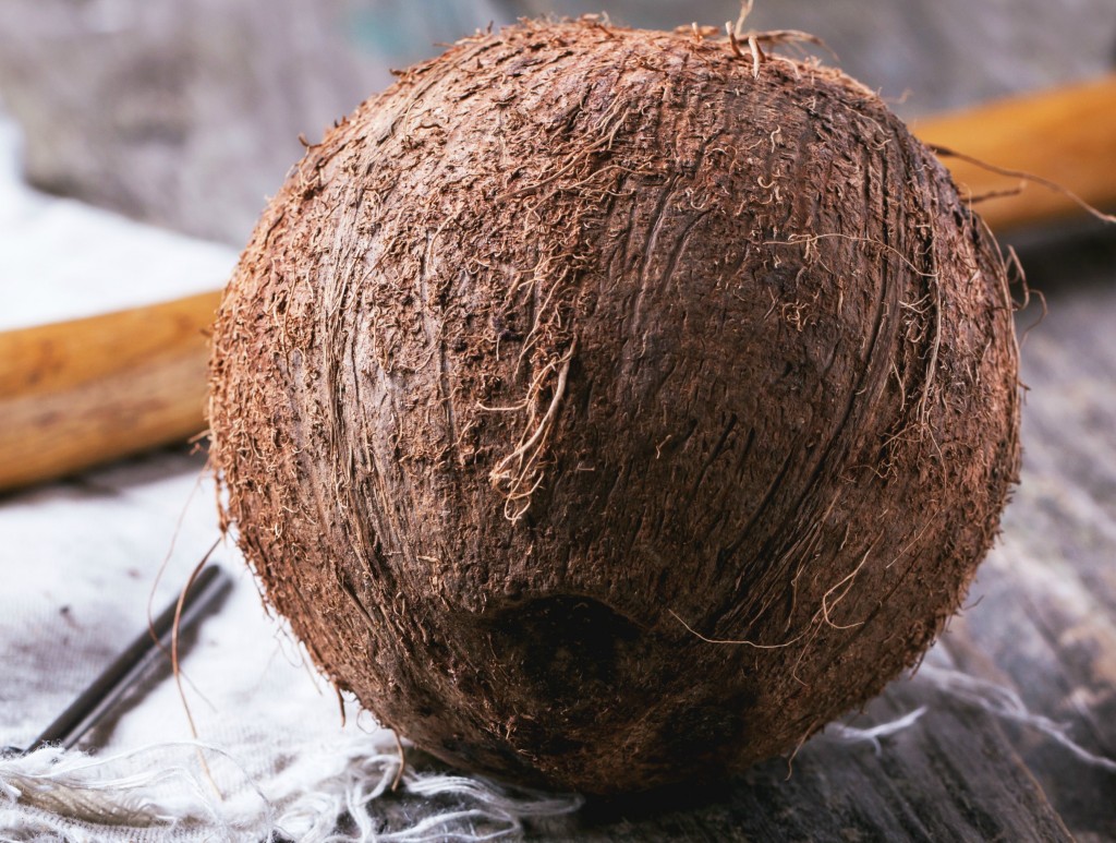 Whole coconut with wooden handle in background
