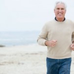 older man in white sweater and jeans running at the beach on an overcast day